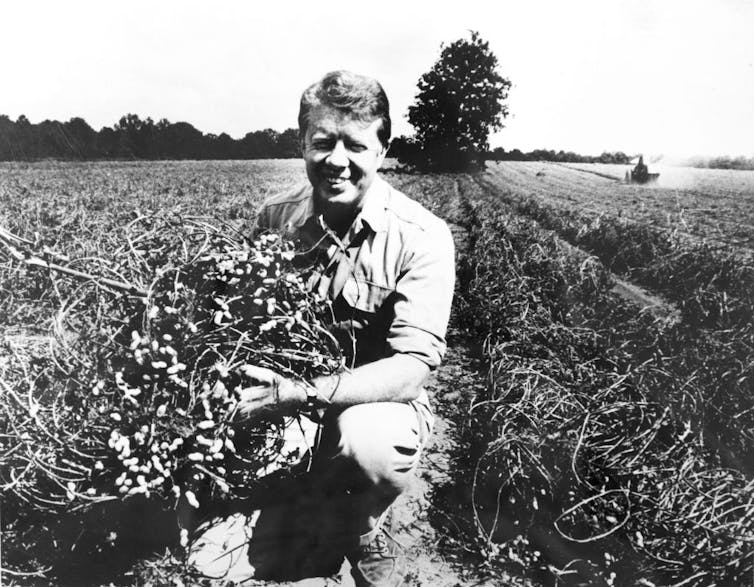 A black and white photo of a man crouching in a field of crops.