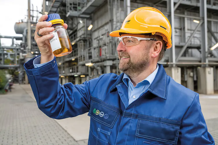 A man in a hard hat and jumpsuit holding a bottle of liquid oil.