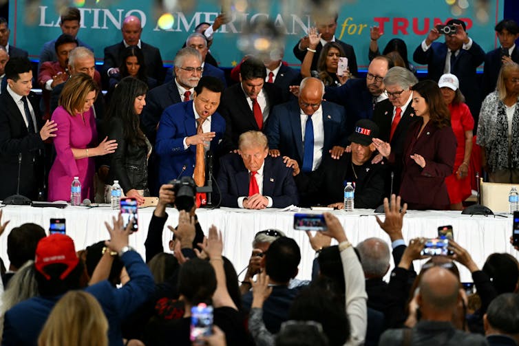Trump prays with his head down, surrounded by other people praying