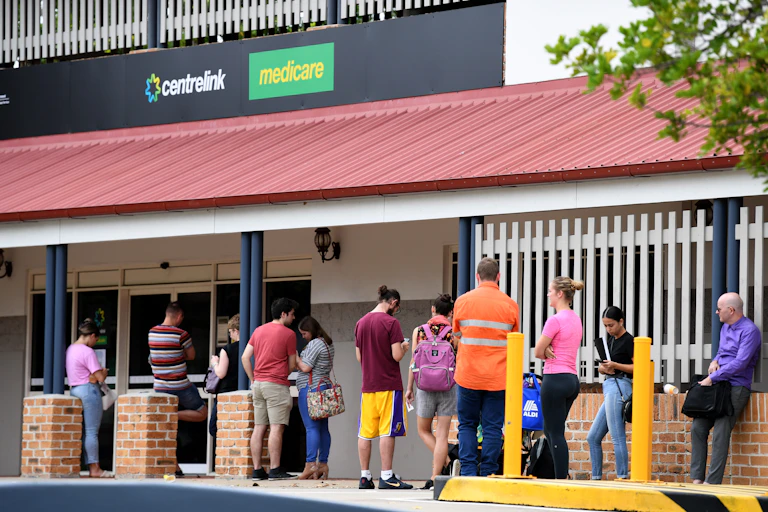 Several people queuing on a strett outside a government services building.