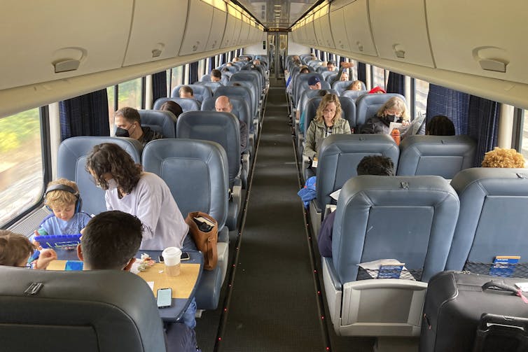 An overview head of people in a train compartment with blue padded seats.