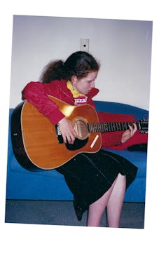 a young woman sitting on a couch playing a guitar