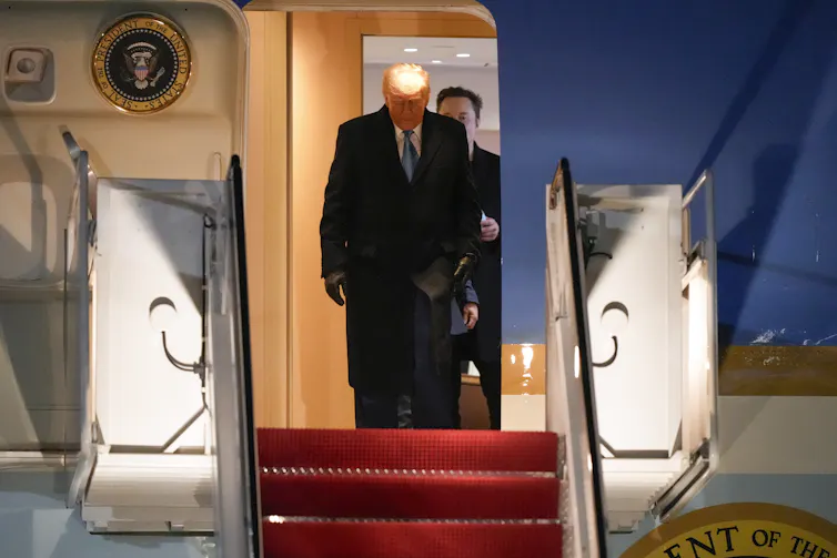 A man in suit debarks a plane with another man standing right behind him.