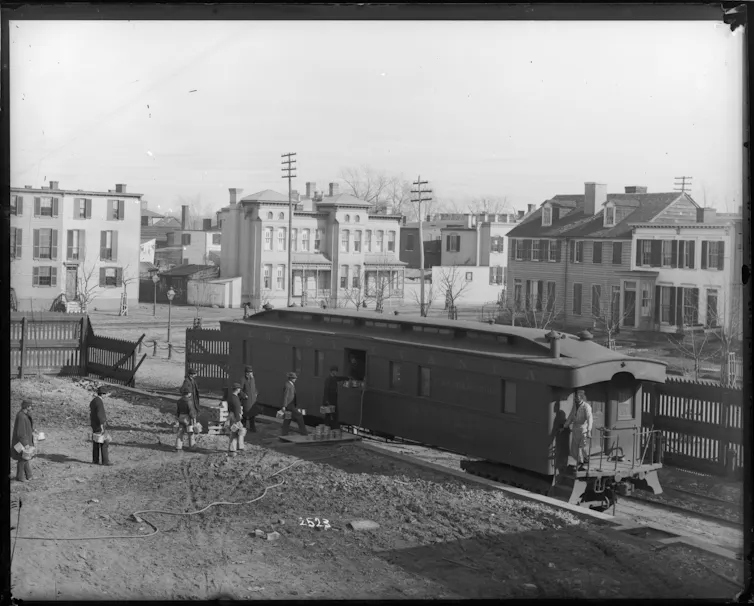 Men stand in line with pails to deposit them in a train car on a siding.