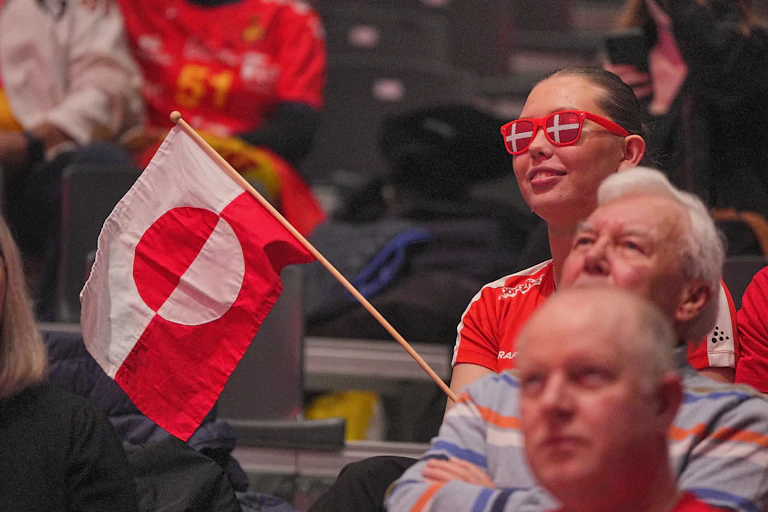 Women wearing glasses with the Danish flag waves a Greenland flag.