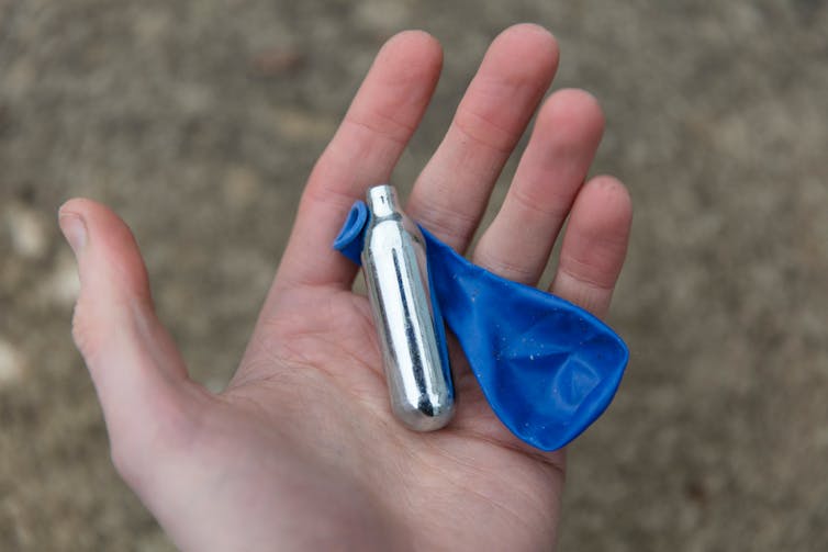 A hand holding a balloon and a silver canister.