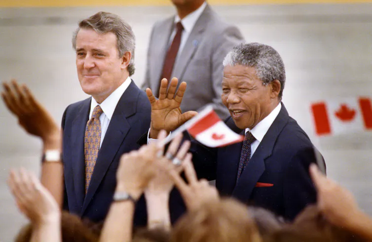 El ex primer ministro canadiense, Brian Mulroni, y el ex presidente de Sudáfrica, Nelson Mandela, dan la bienvenida a las personas que agitan las banderas canadienses.