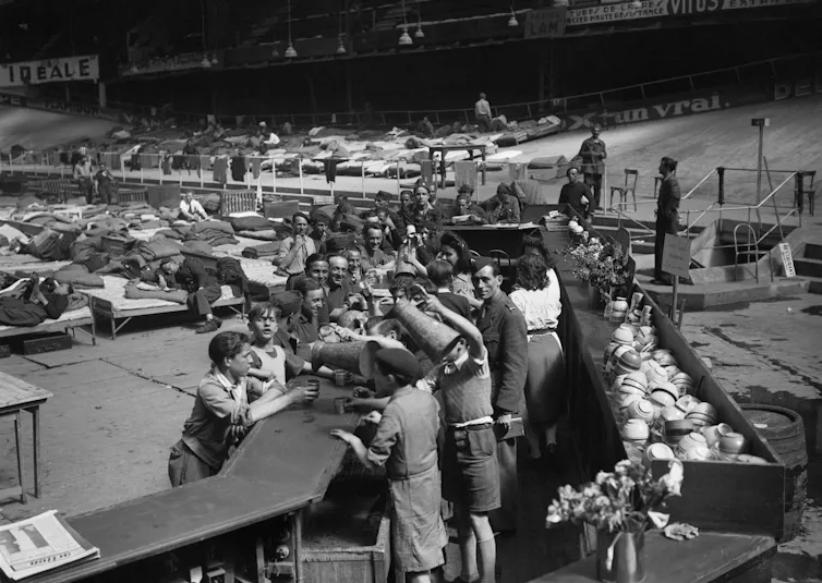 Des enfants et des femmes servent des boissons aux prisonniers de guerre français en avril 1945 au centre d’accueil des prisonniers du Vel d’Hiv à Paris, à leur retour d’Allemagne à la fin de la Seconde Guerre mondiale