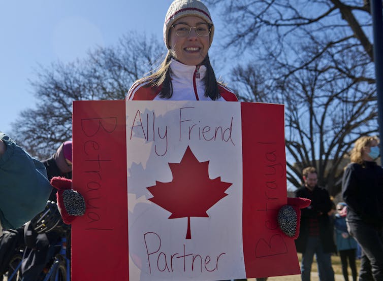 A person holds a sign decorated like the Canadian flag.