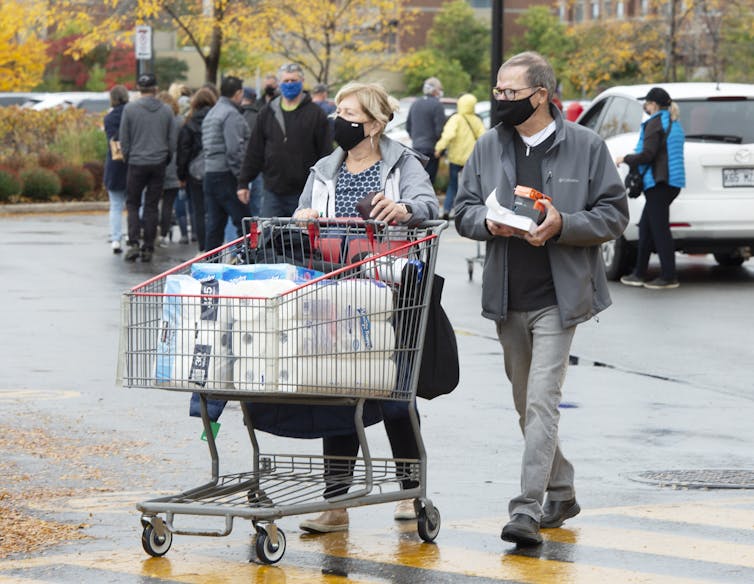 A woman in a face mask pushes a shopping cart full of toilet paper in a parking lot