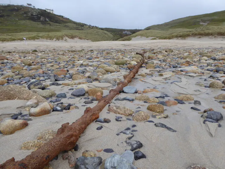 Long rusted cable running along a pebbly beach.