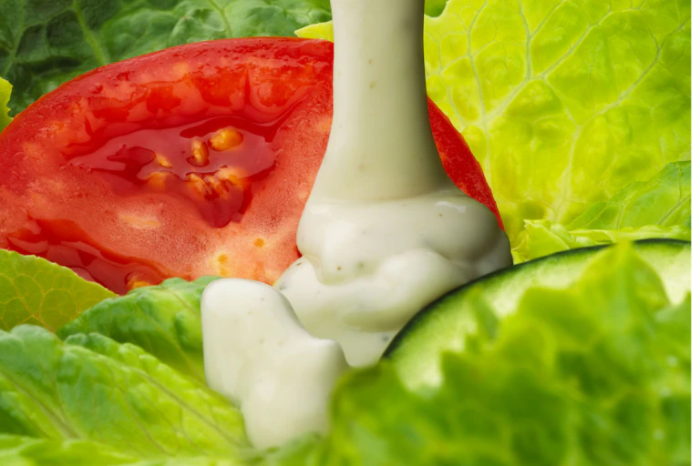 stream of white dressing flows down onto a salad