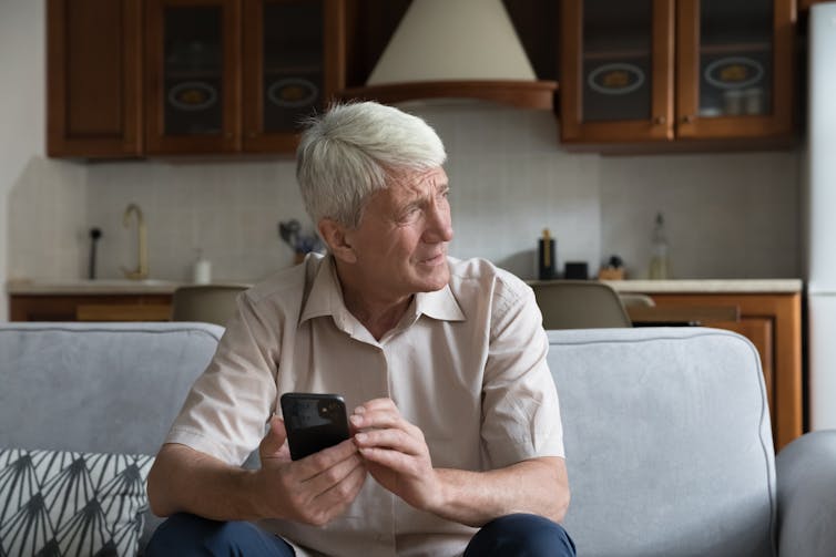 An older person looks out the window while holding their phone.