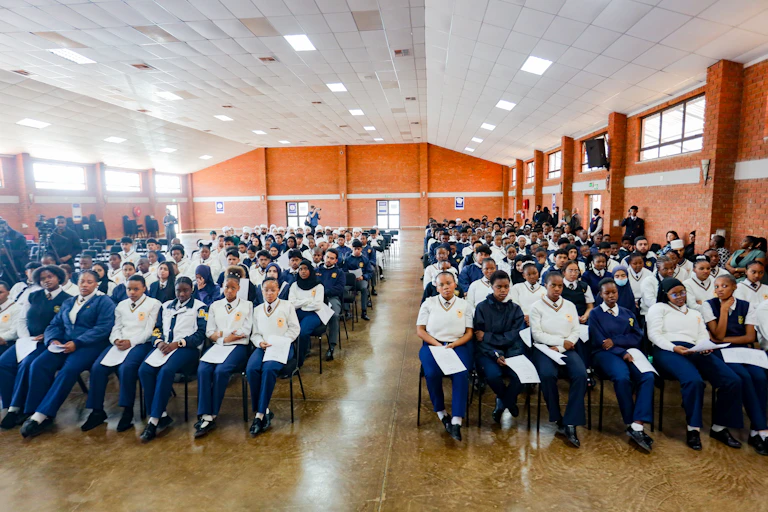 A school hall filled with young people in uniforms, all holding pieces of paper in their laps