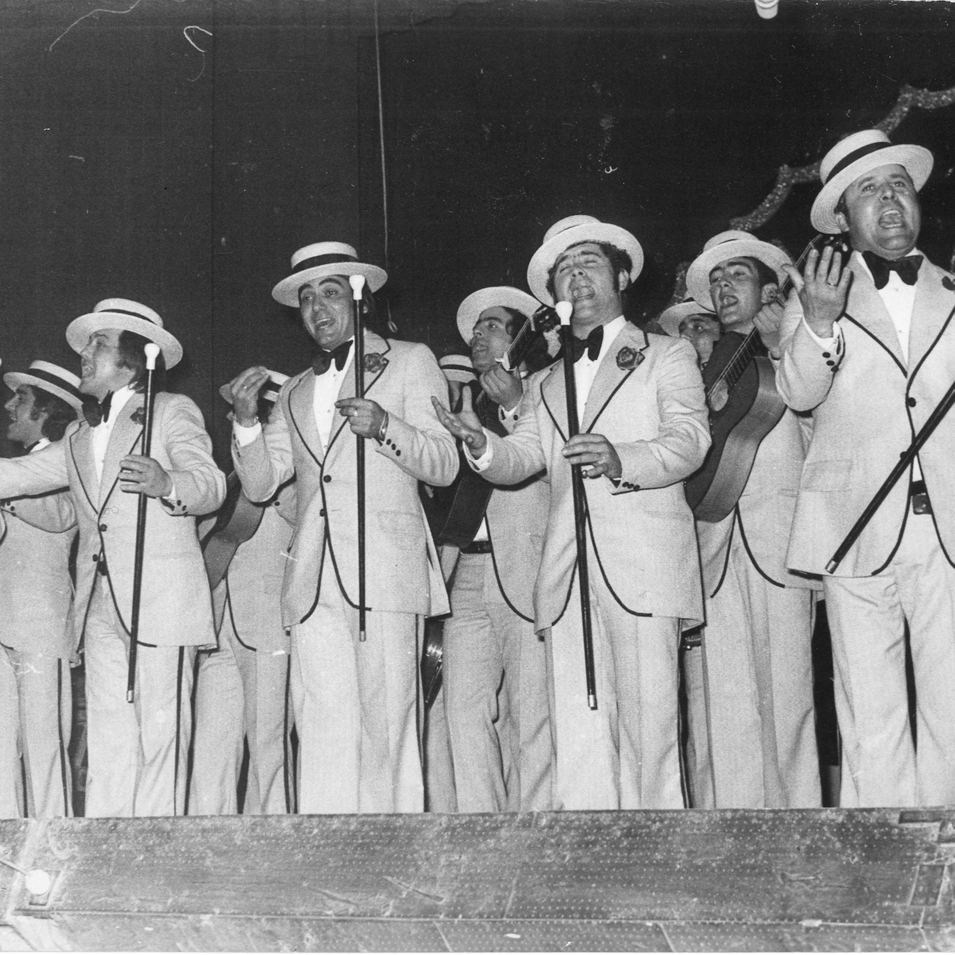 Un grupo de hombres trajeados y cantando delante de unos micrófonos.