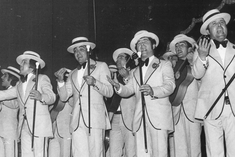 Un grupo de hombres trajeados y cantando delante de unos micrófonos.