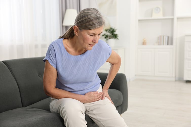 Woman sitting on a sofa, holding her hip in pain.
