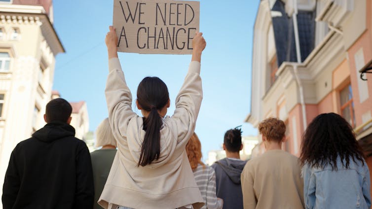 Young protesters were seen from behind, reading a mark with a young woman in a white shirt 'we need to change'