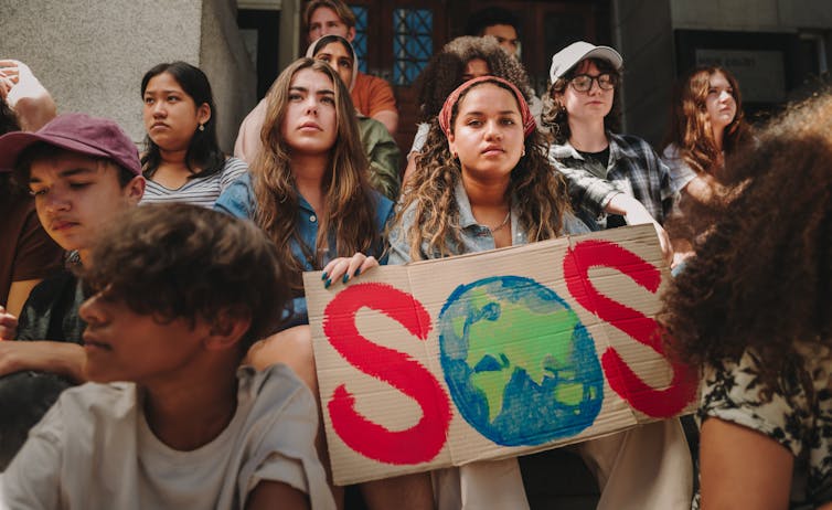 Young people at a climate change rally holding a sign reading 'SOS' with the earth in place of the O