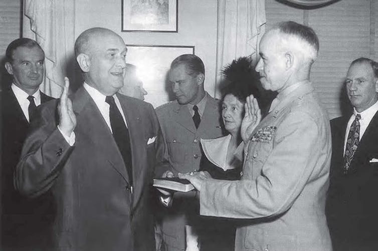 A man in a suit and tie stands facing a man in a military uniform.