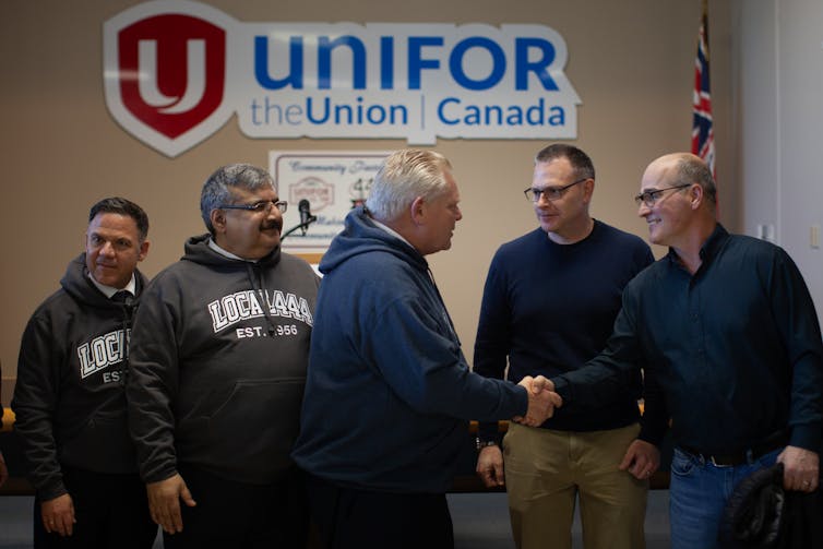 El hombre blanco de mediana edad sacudió a otro hombre blanco frente a un letrero que dice uniforme