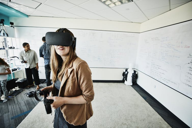 A woman wearing a black VR headset, which looks like a large, bulky pair of glasses with no lenses.