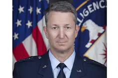 A man in uniform poses in front of a U.S. flag and a CIA flag.