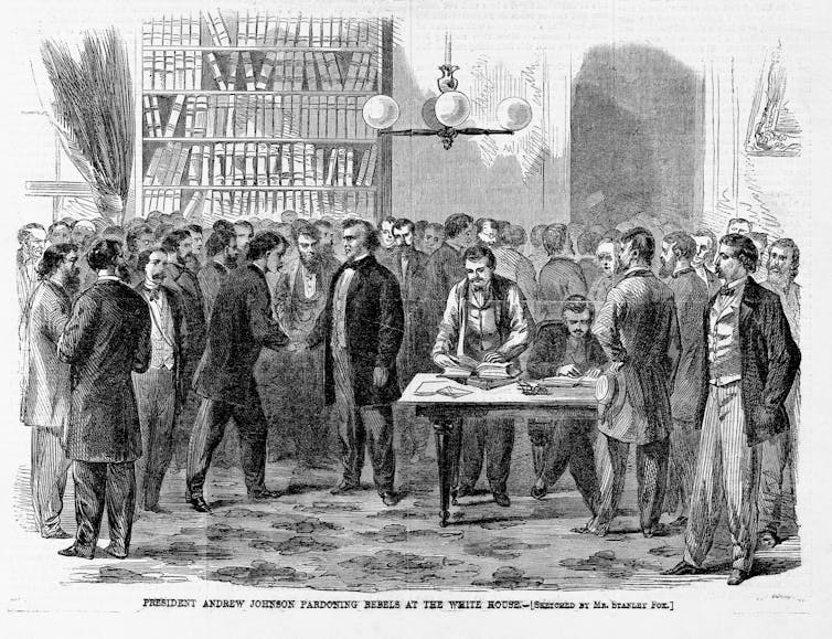 People in formal dress gather, and one of them in the center shakes hands with another.