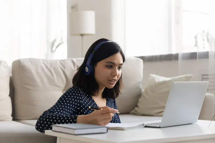 A woman wearing headphones looking at a laptop screen