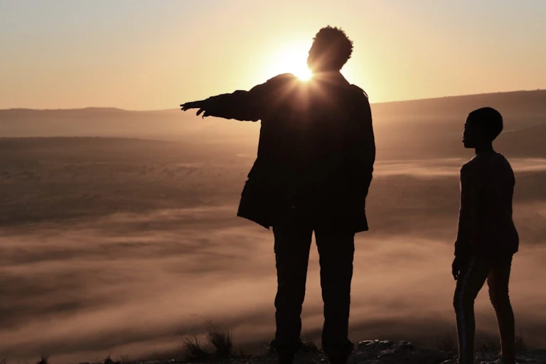 A woman and a girl in silhouette as the stand on a mountain, the sun rising.