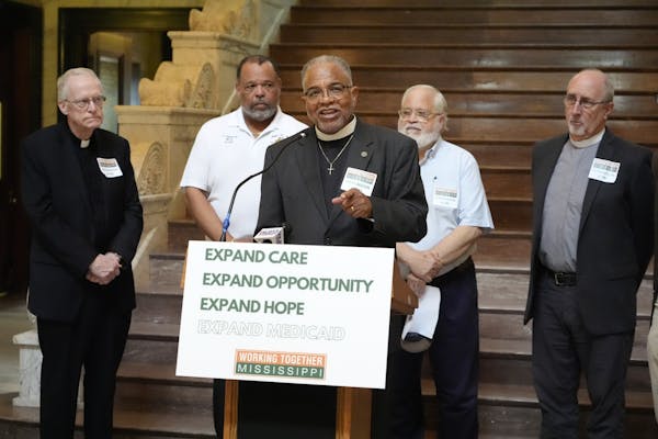 Religious men, some in collars, stand together around a sign calling for Medicaid expansion in Mississippi.