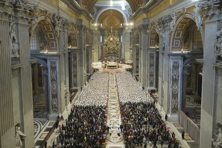 A huge, ornately decorated cathedral with many rows of people in white outfits sitting in the middle.