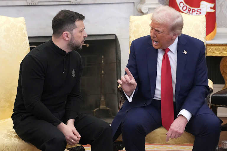 Two men sitting in yellow chairs, with one looking angry and pointing his finger at the other.