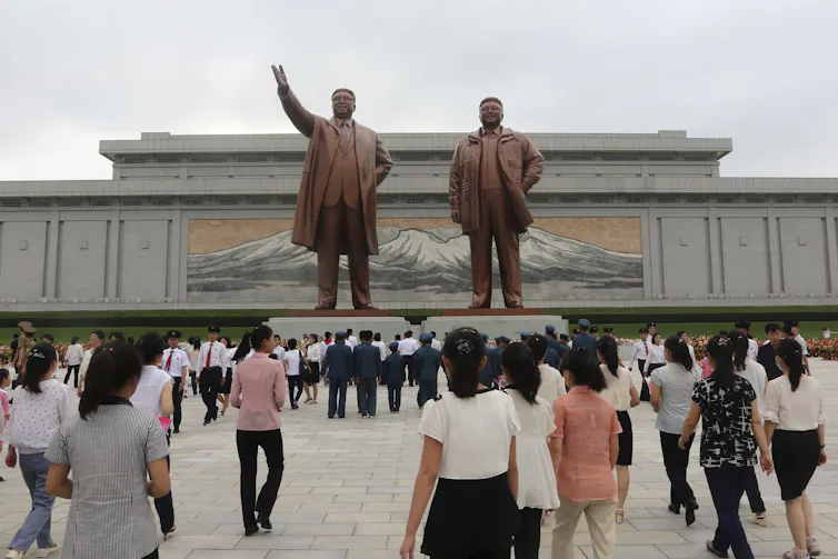 North Koreans gather in a public square and look at two tall statues