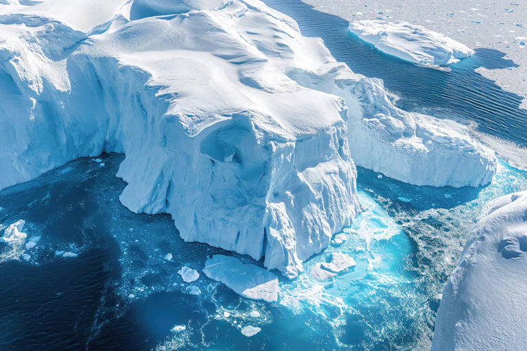 An aerial perspective showcases the dramatic melting icebergs of Antarctica, where the vivid blue sea claims the collapsing icy giants, a poignant visual testament to climate change