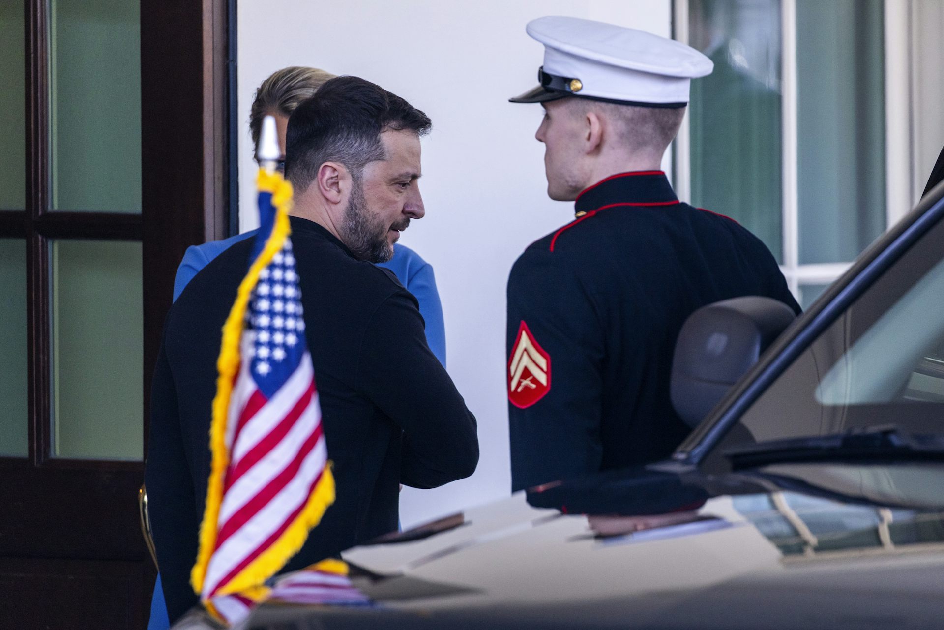 Ukrainian president, Volodomyr Zelensky, leaves the White House. In the foreground is a US military officer in dress uniform.