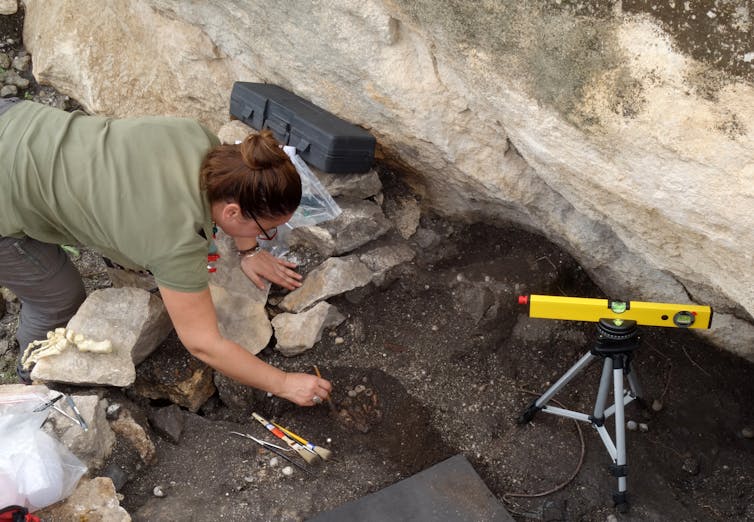 A person working with small bones in a pit alongside some scientific equipment