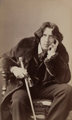 Queer theatre within the nineteenth century was once a spot of codes, cross-dressing and blackmail 3 Oscar Wilde in a fur coat wearing a large ring