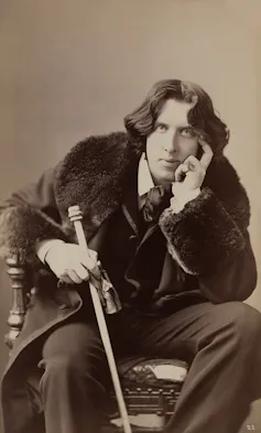Oscar Wilde in a fur coat wearing a large ring
