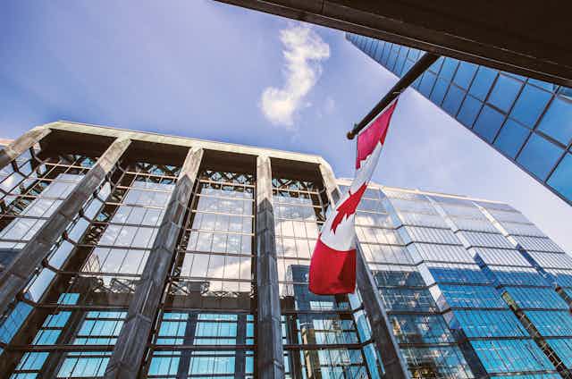 Upward shot of a glass-fronted office building with a Canadian flag flying in front