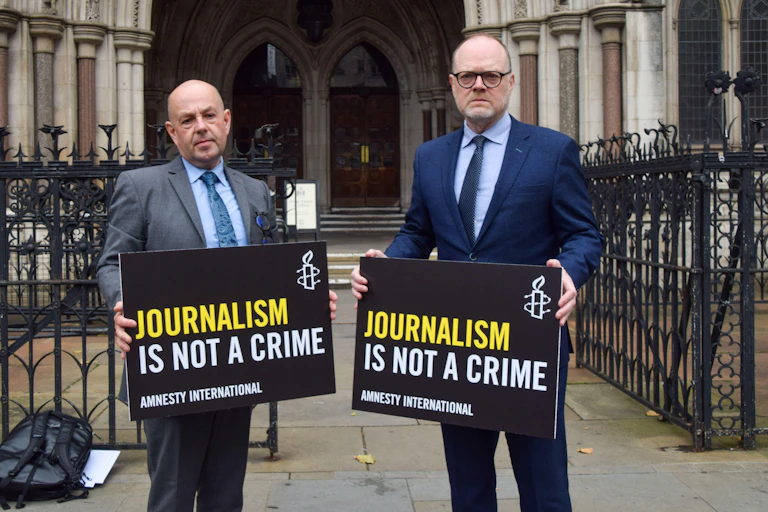 McCaffrey and Birney holding signs reading 'journalism is not a crime' outside the royal courts of justice