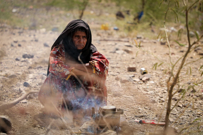displaced yemeni woman sitting on the ground making food.