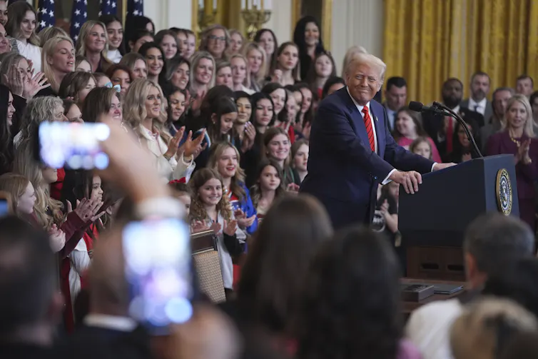 A man seen addressing a crowd of people, many of whom appear to be young women or girls.