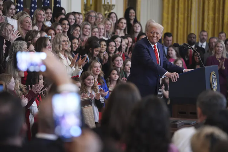 A man seen addressing a crowd of people, many of whom appear to be young women or girls.