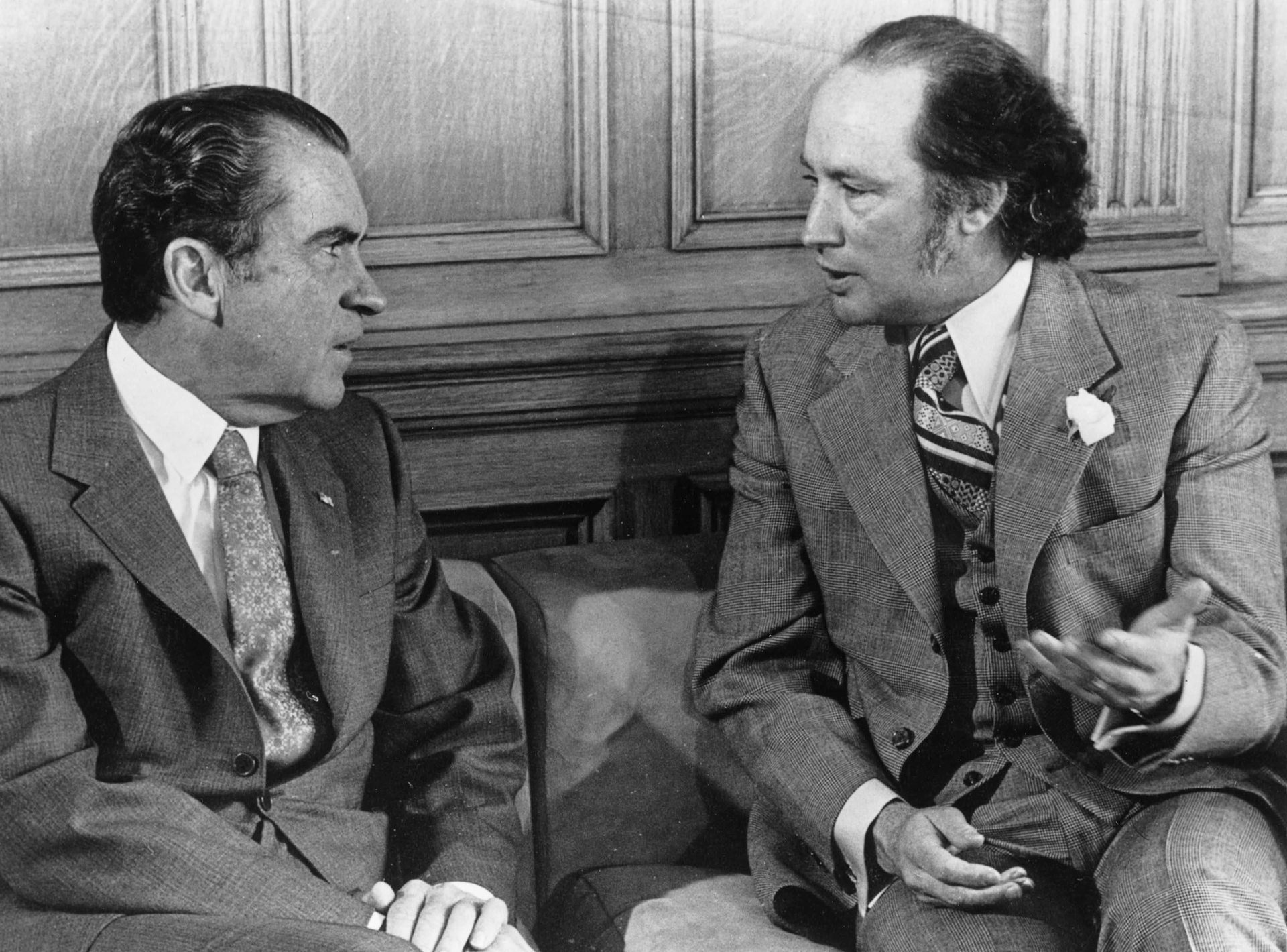 El presidente Richard Nixon y el primer ministro Pierre Trudeau se sientan en sillas uno frente al otro mientras hablan.