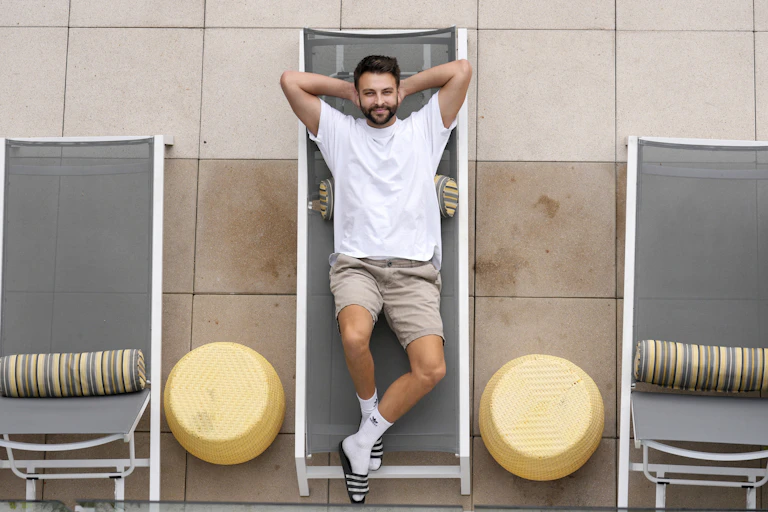 Bearded man in a white T-shirt lies on a poolside lounge chair that's part of a tasteful selection of outdoor furniture.