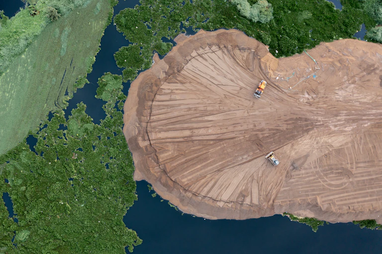 aerial shot of green land, rivers and brown sandy mined area with two lorries