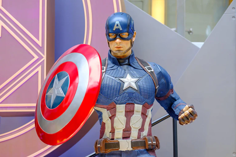 A man in a blue outfit with an 'A' on his hat holds a red and white shield with a star.