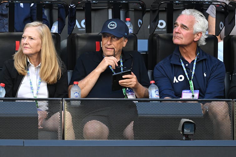 Bill Gates wears a blue cap while watching the tennis.