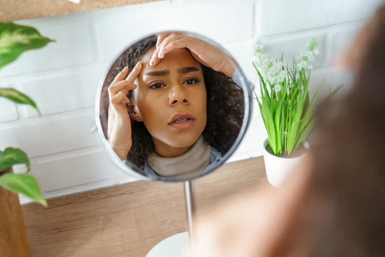 A teenage girl pulls up her eyebrow with her finger while looking into a mirror